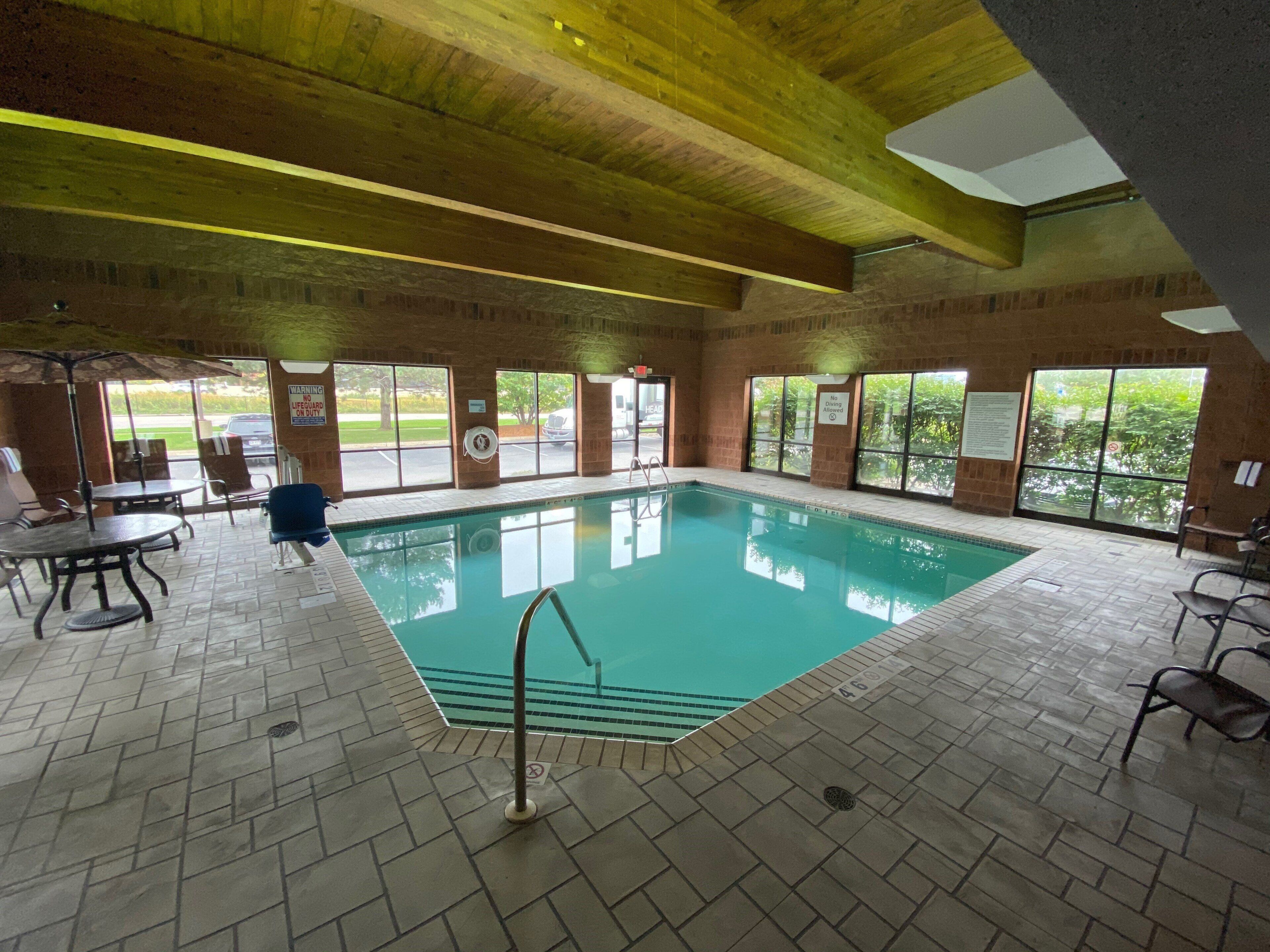 Una piscina interior con suelo de baldosas, una escalera de piscina y vistas al exterior a través de amplias ventanas.