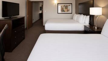 A hotel room with two beds, a TV, a desk with a lamp, and a painting on the wall.