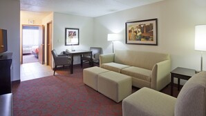 Una habitación de hotel con sofá, otoman, mesa de comedor con sillas, lámpara y un cuadro en la pared.