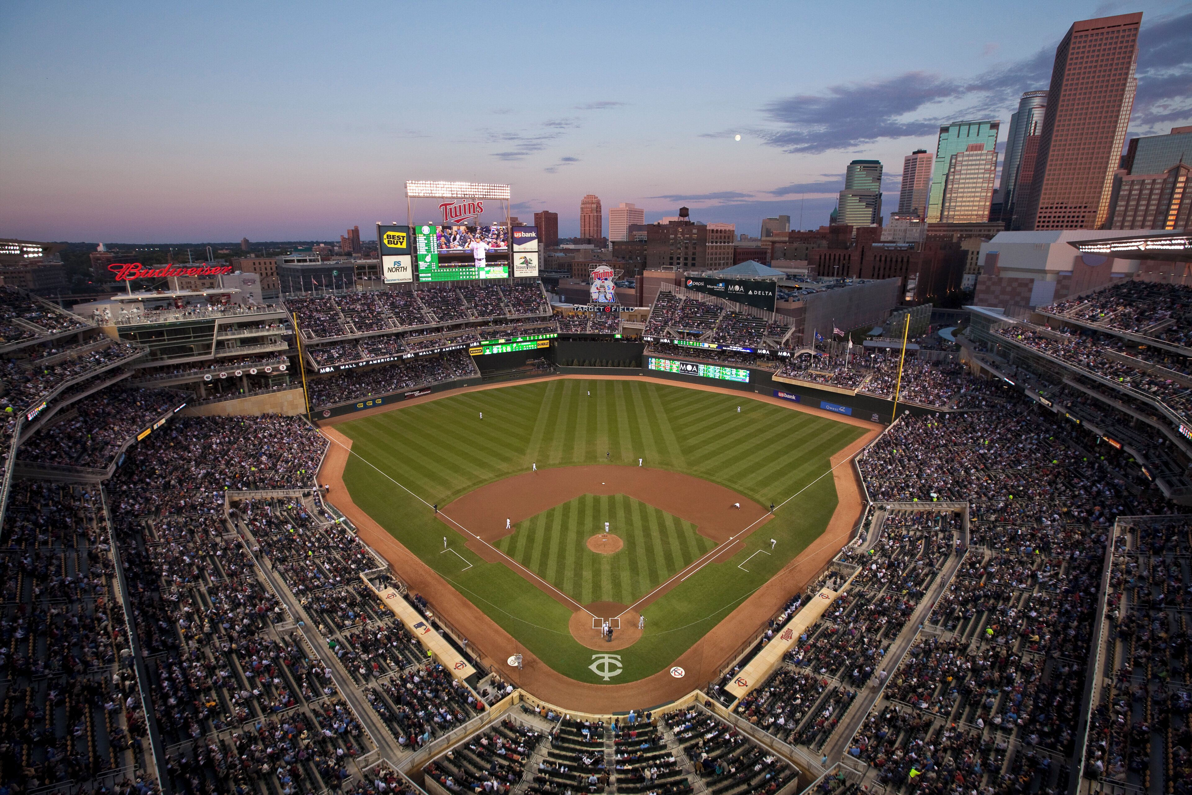 A baseball stadium with multiple levels of seating and a large screen displaying game information.