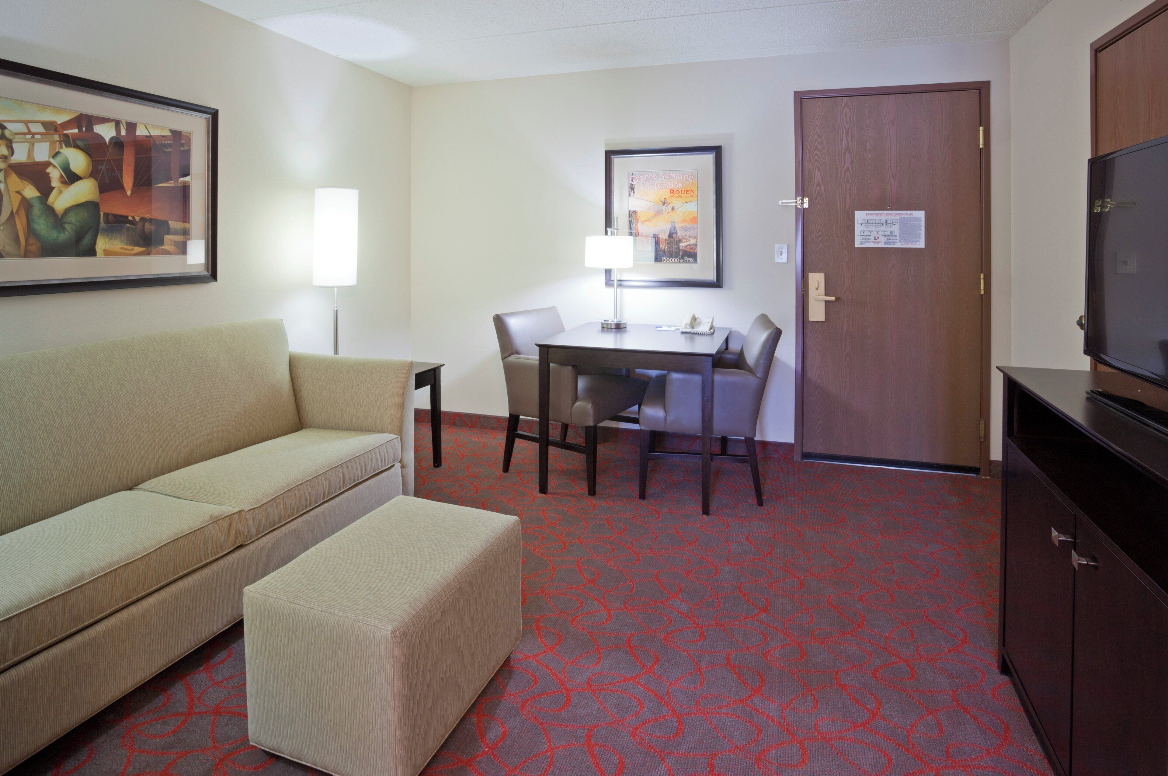 A hotel room with a sofa, a small table, a desk, and a television.