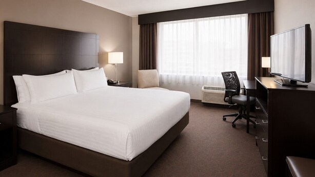 Una habitación de hotel con una cama grande, un escritorio con silla, televisión y ventana con cortinas.