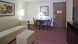 Una habitación de hotel con sofá, una mesita, una mesa de comedor con sillas, televisión y una puerta.