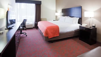 Una habitación de hotel con una cama, un escritorio con televisor, una silla, una lámpara y un teléfono en la mesita de noche.