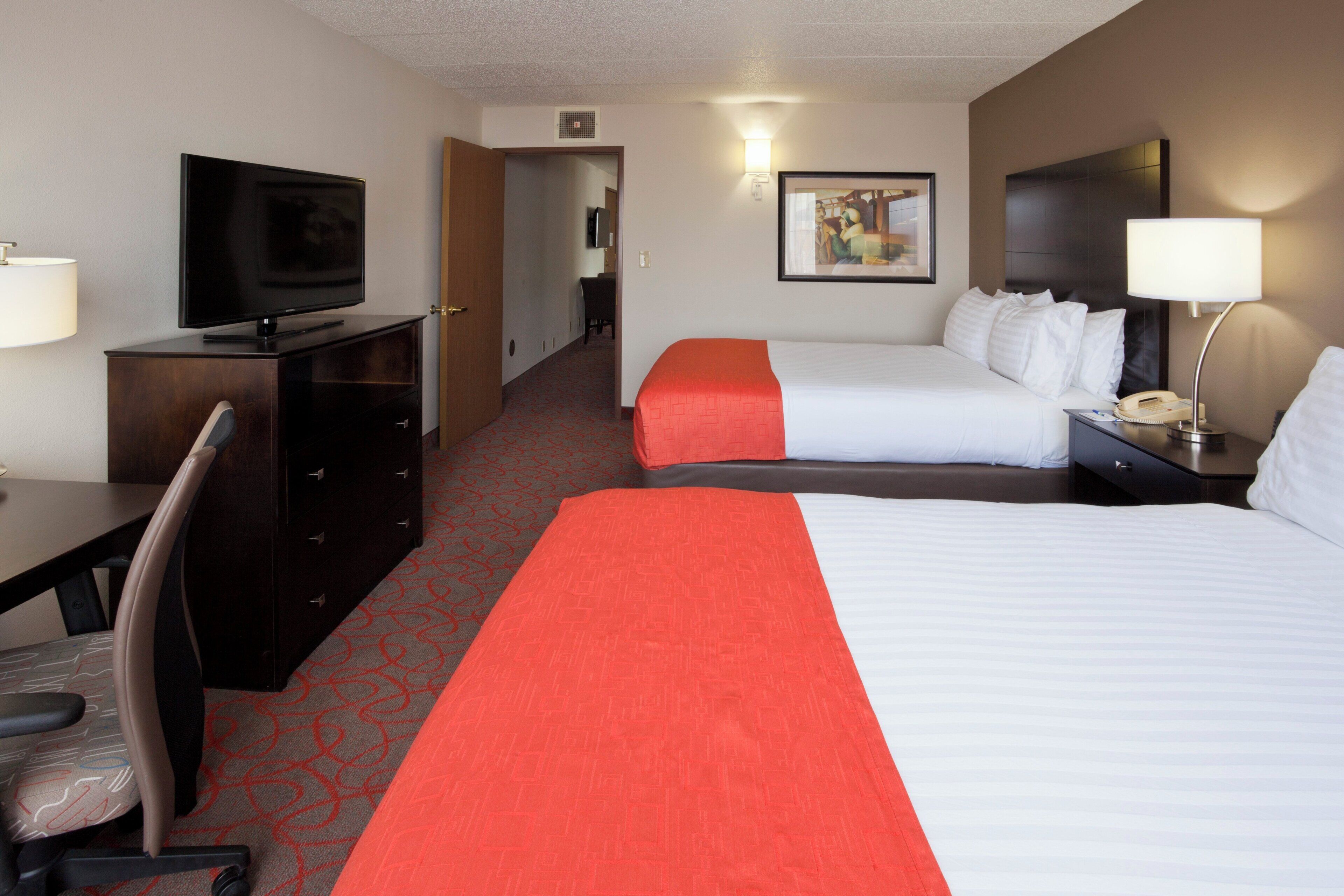 A hotel room with a TV, two beds, a desk, and a chair.