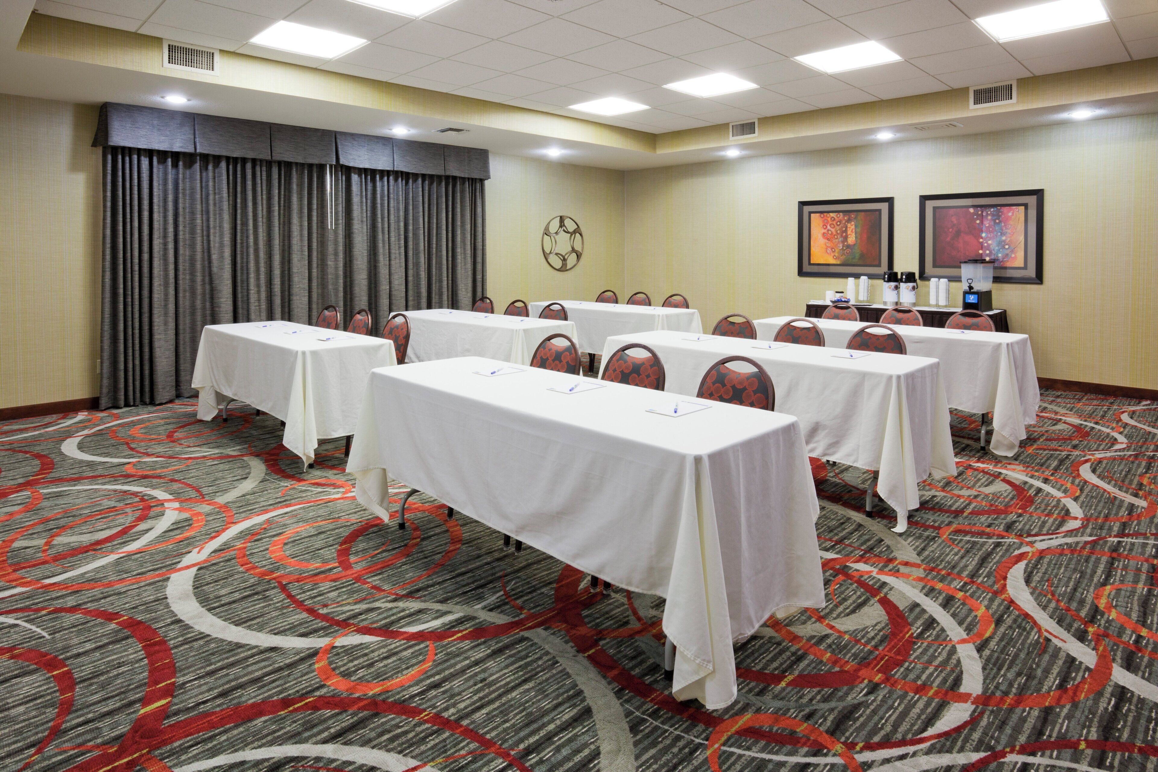 A conference room with multiple tables and chairs, a patterned carpet, and artwork on the walls.
