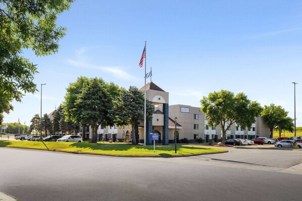 A hotel with a central tower, parking lot, and surrounding greenery.