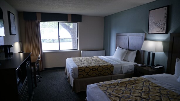 Una habitación de hotel con dos camas, un escritorio, una silla, una lámpara y una ventana con cortinas.