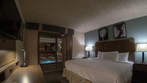 Una habitación de hotel con una cama grande, lámparas de noche, un escritorio con lámpara y una televisión en la pared.