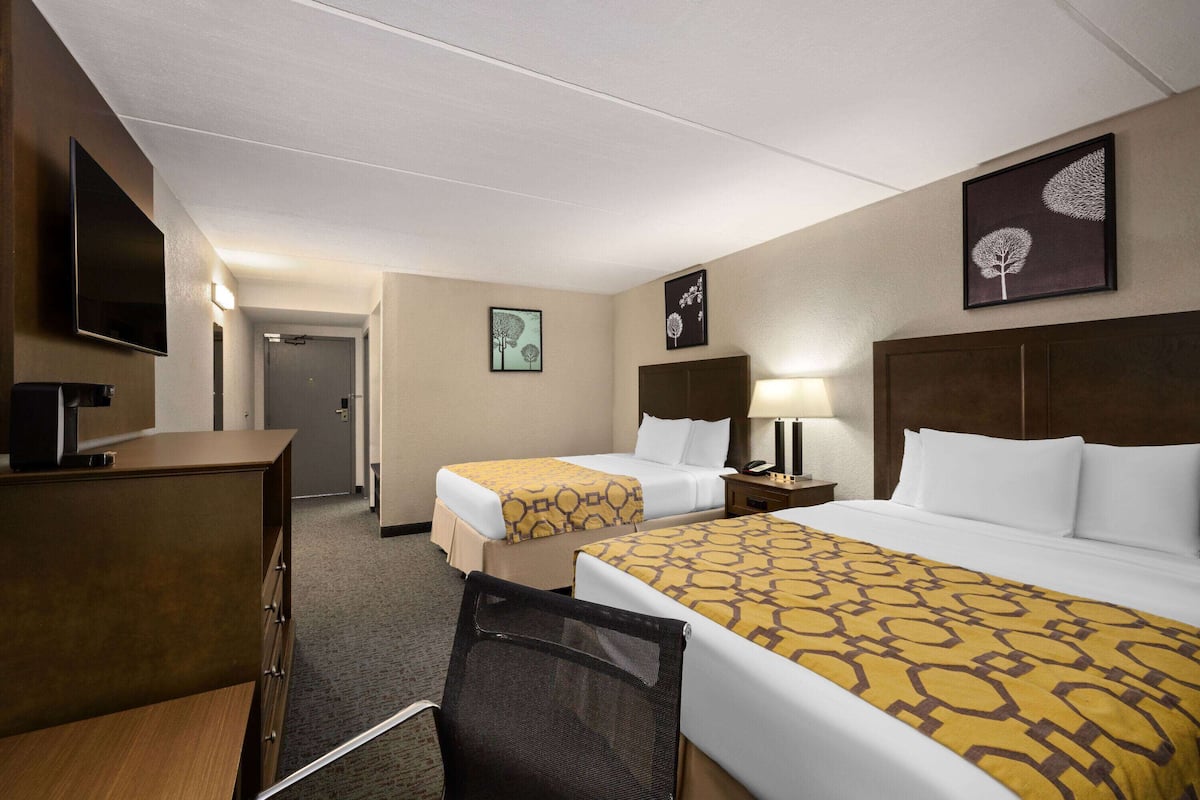 Habitación de hotel con dos camas, un escritorio, un televisor y obras de arte en las paredes.