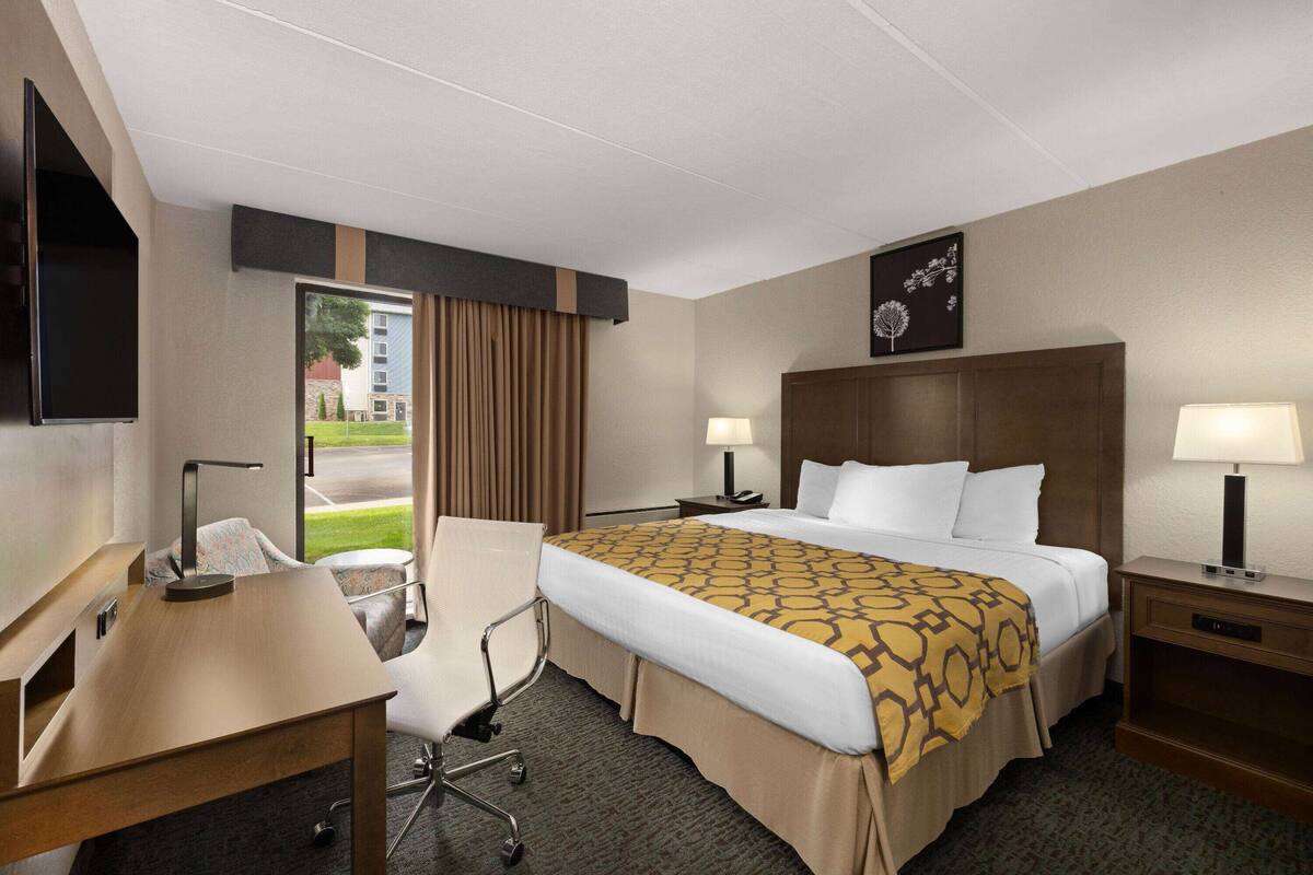 Habitación de hotel con cama, escritorio, silla, dos mesitas de noche con lámparas, televisión y ventana con cortinas.
