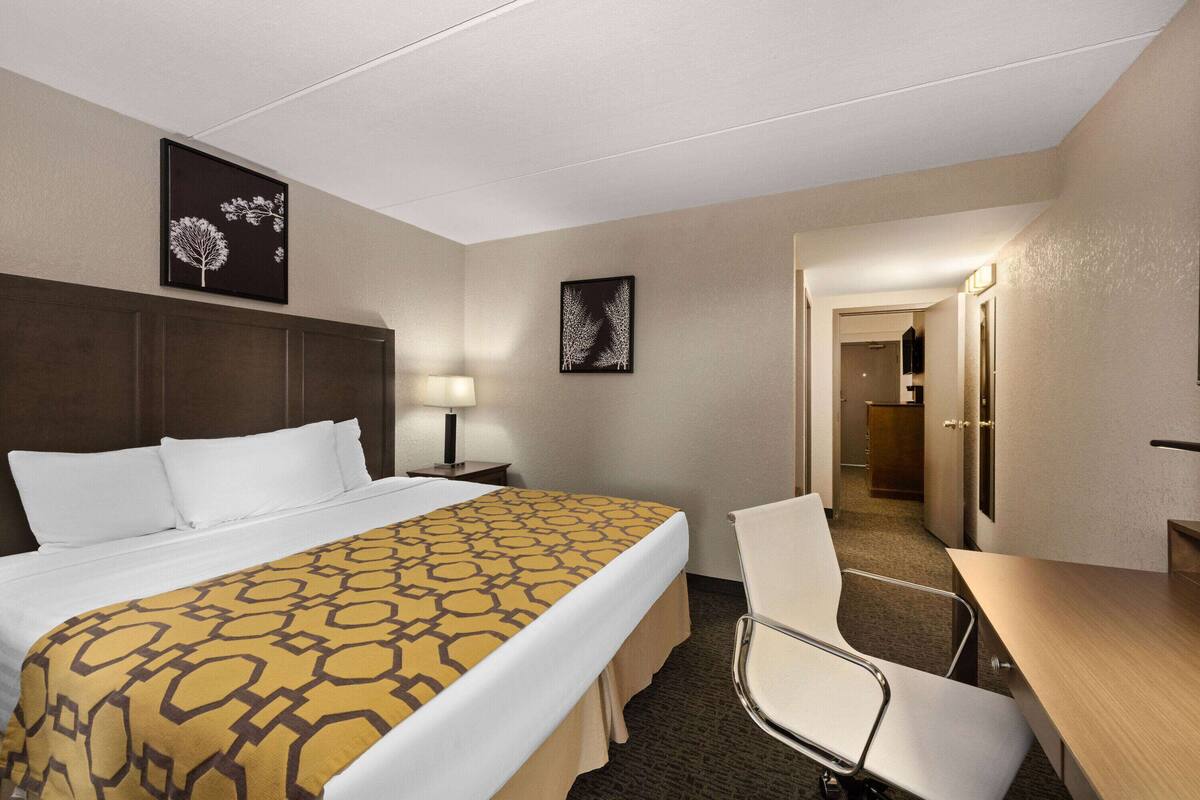Habitación de hotel con cama, escritorio, silla, mesita de noche y dos obras de arte colgadas en la pared.