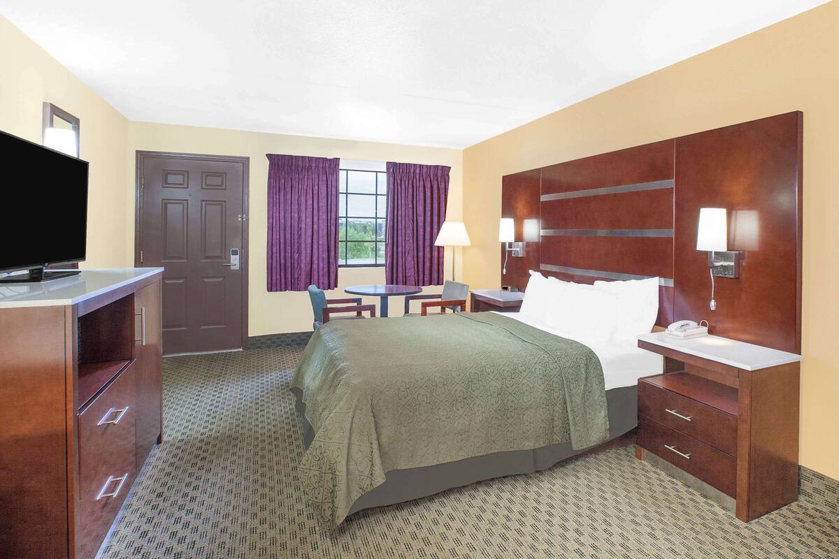 A hotel room with a bed, a desk, a chair, a television, a lamp, and a door.