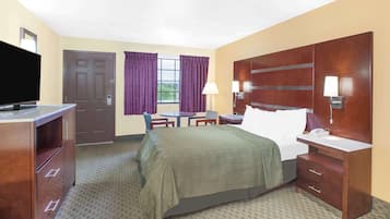 A hotel room with a bed, a desk, a chair, a television, a lamp, and a door.