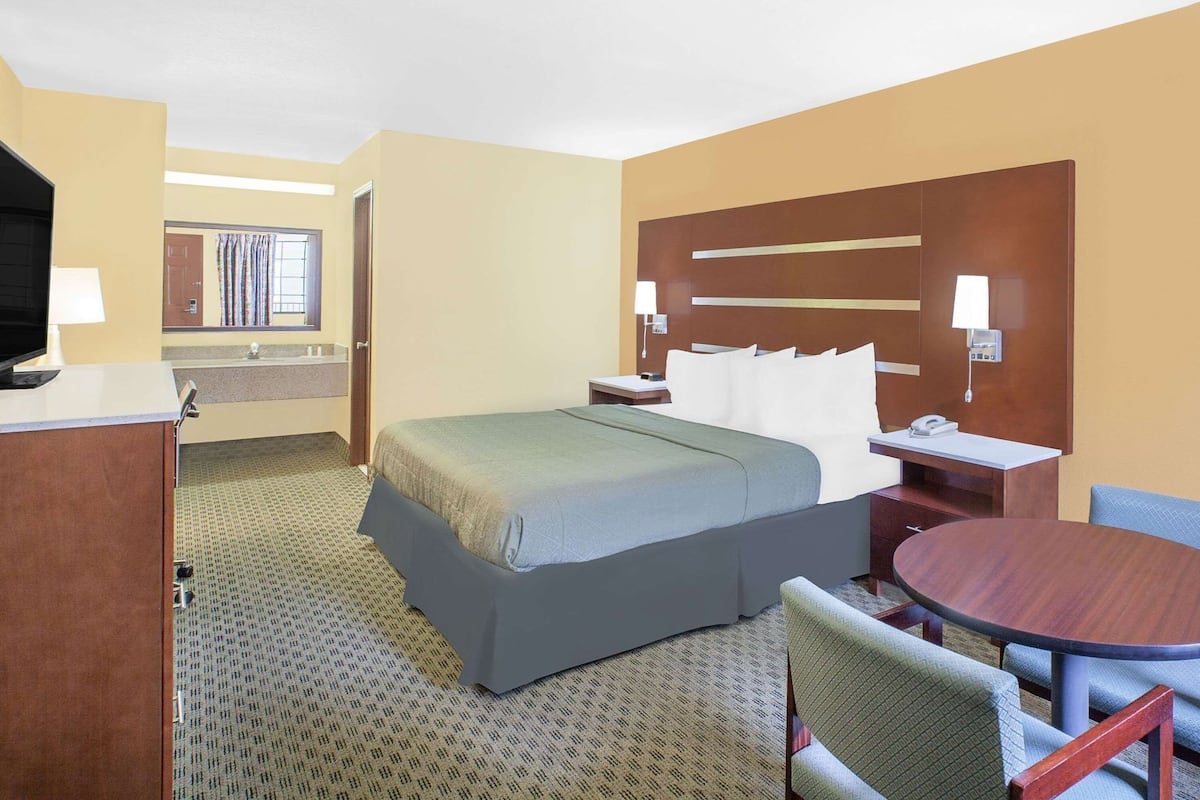 A hotel room with a bed, bedside tables, a desk, a chair, and a small table.