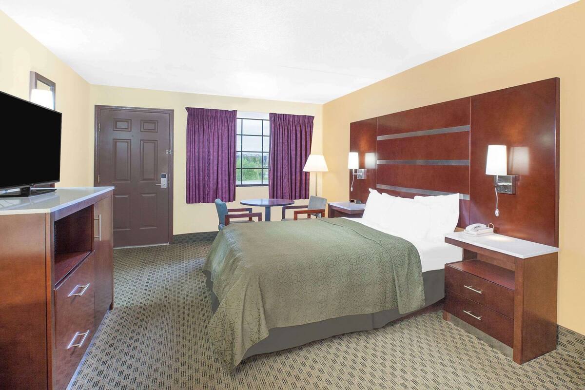 A hotel room with a bed, a desk, a chair, a TV, and a window with curtains.
