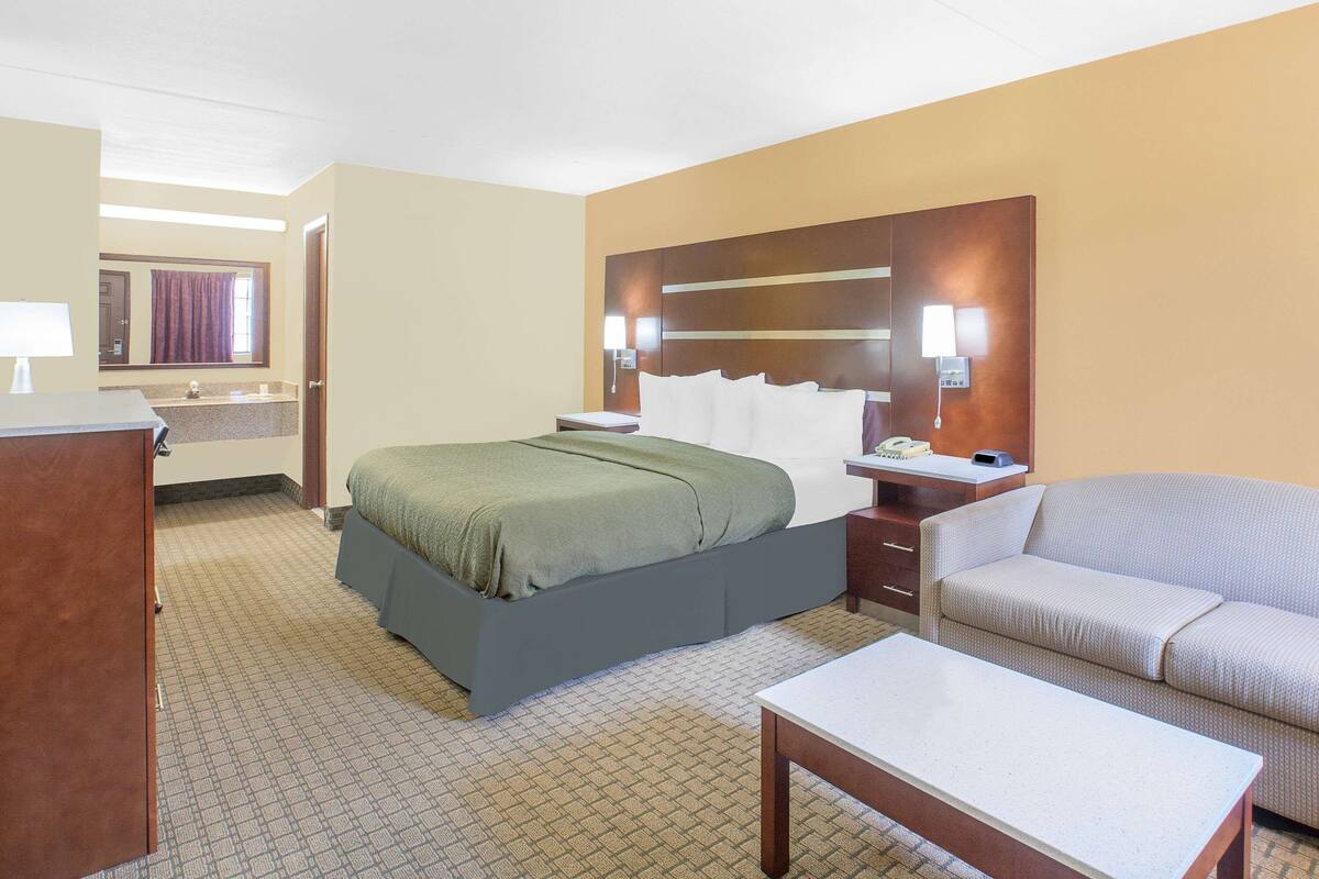 A hotel room with a bed, a sofa, a desk, and a mirror.