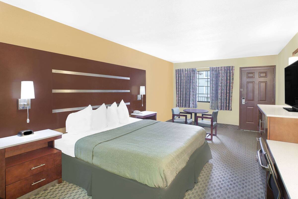 A hotel room with a bed, bedside table, lamp, desk, chair, and a television.