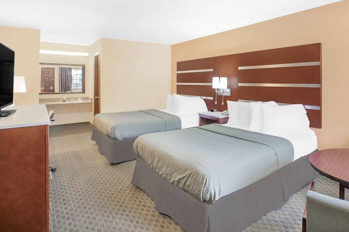 A hotel room with two beds, a desk, a TV, a mirror, and a small table.