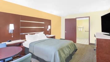 Habitación de hotel con una cama, mesitas de noche, un escritorio, una silla, un televisor y un baño visible a través de una puerta abierta.