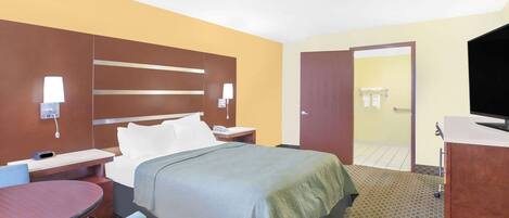 Habitación de hotel con una cama, mesitas de noche, un escritorio, una silla, un televisor y un baño visible a través de una puerta abierta.