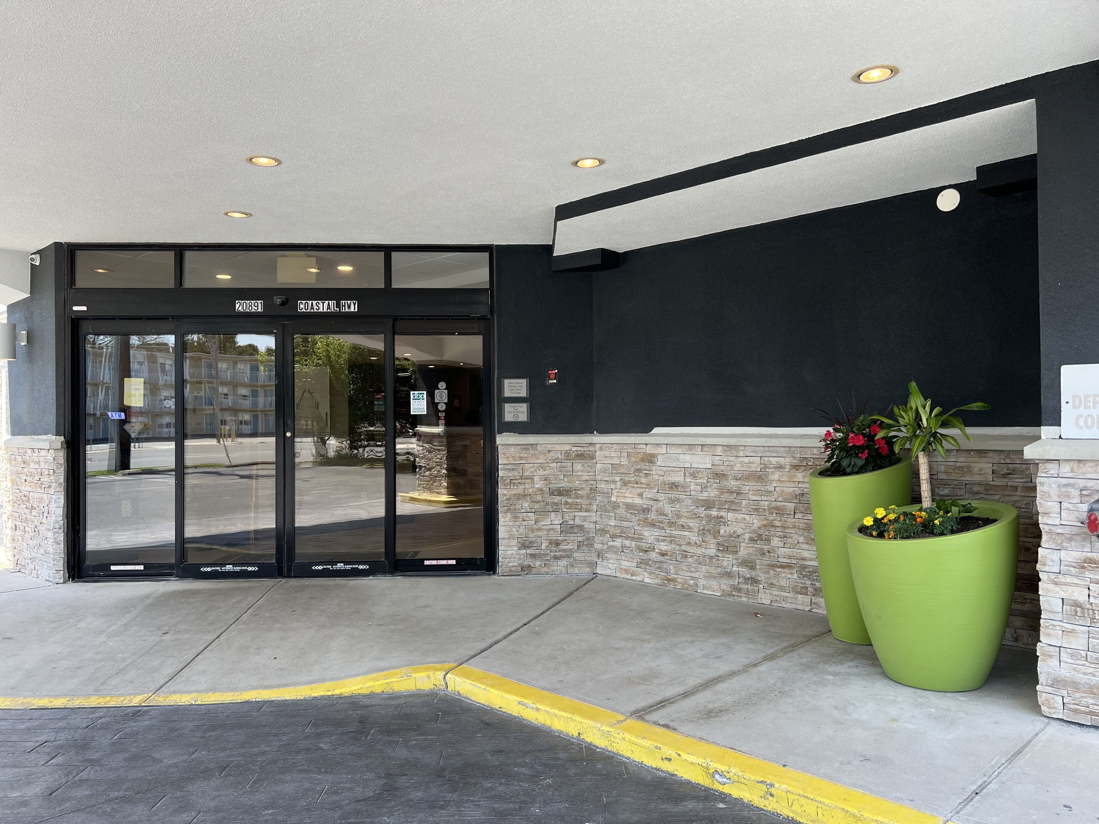 A hotel entrance with a glass door, a stone wall, and two large green planters.