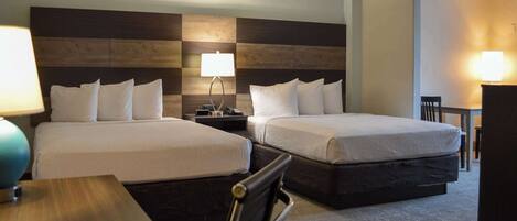 A hotel room with two beds, a desk, and a chair.