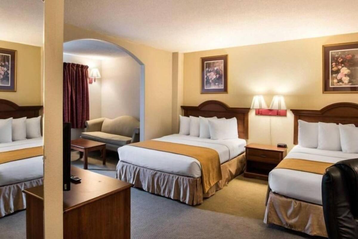 A hotel room with three beds, a desk, a chair, and two lamps.