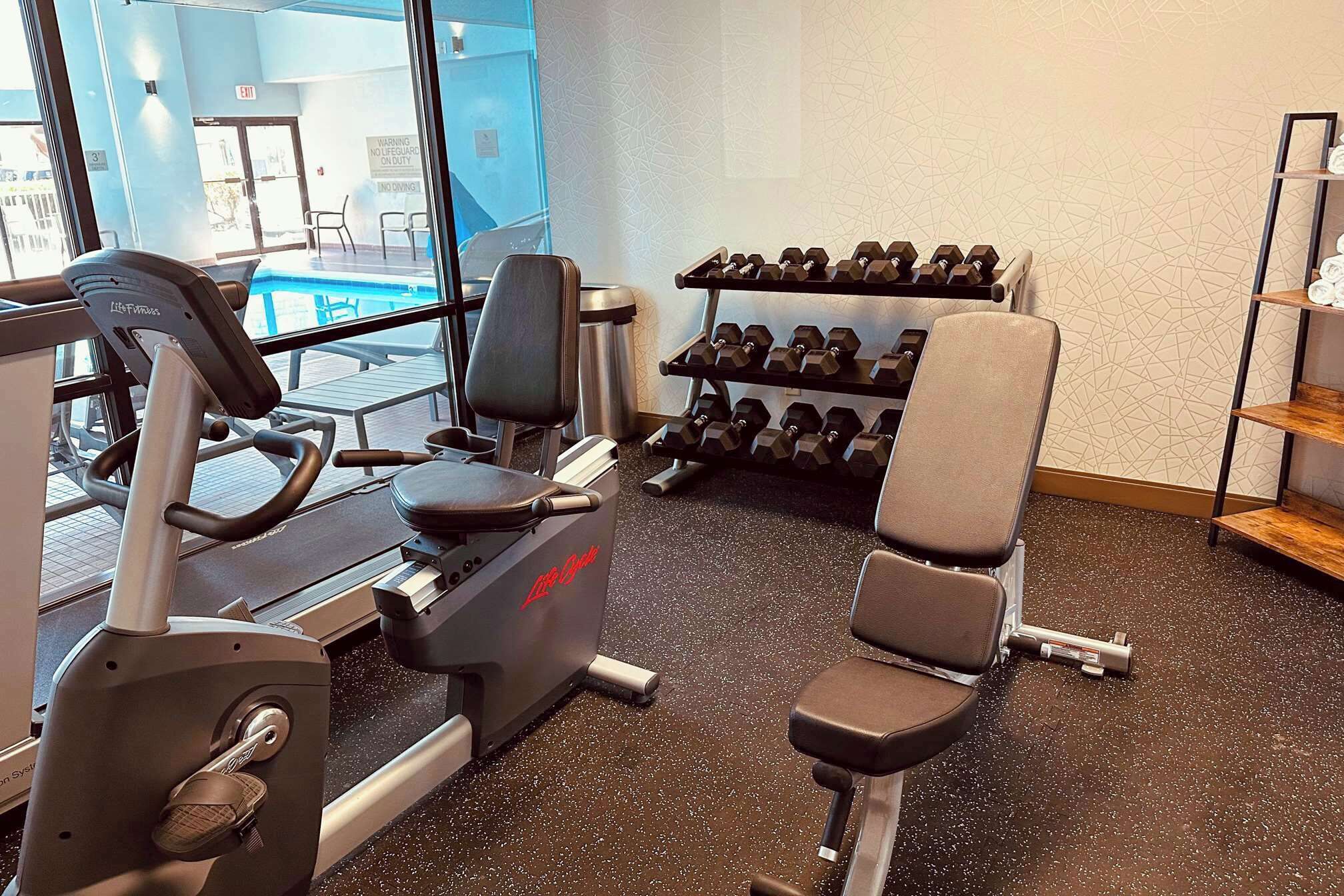 Un gimnasio con equipo de cardio, mancuernas y una silla.