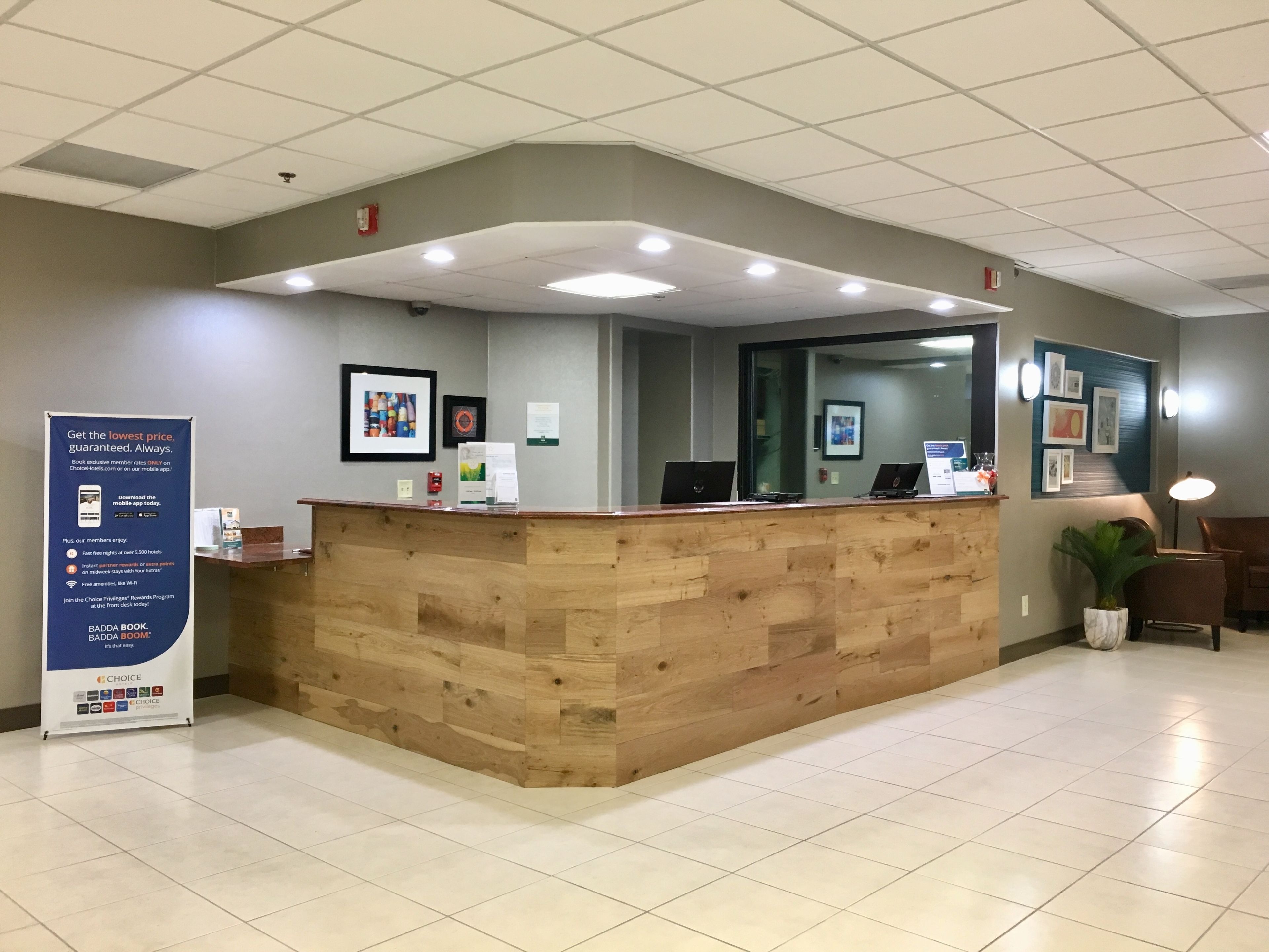 Un área de recepción con un mostrador de madera, un cartel informativo azul y piso de baldosas.