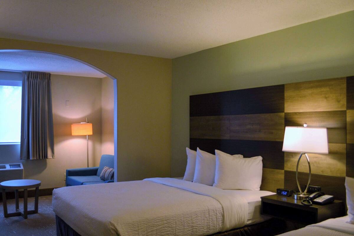 A hotel room with a bed, a desk, a chair, a nightstand, and a lamp.