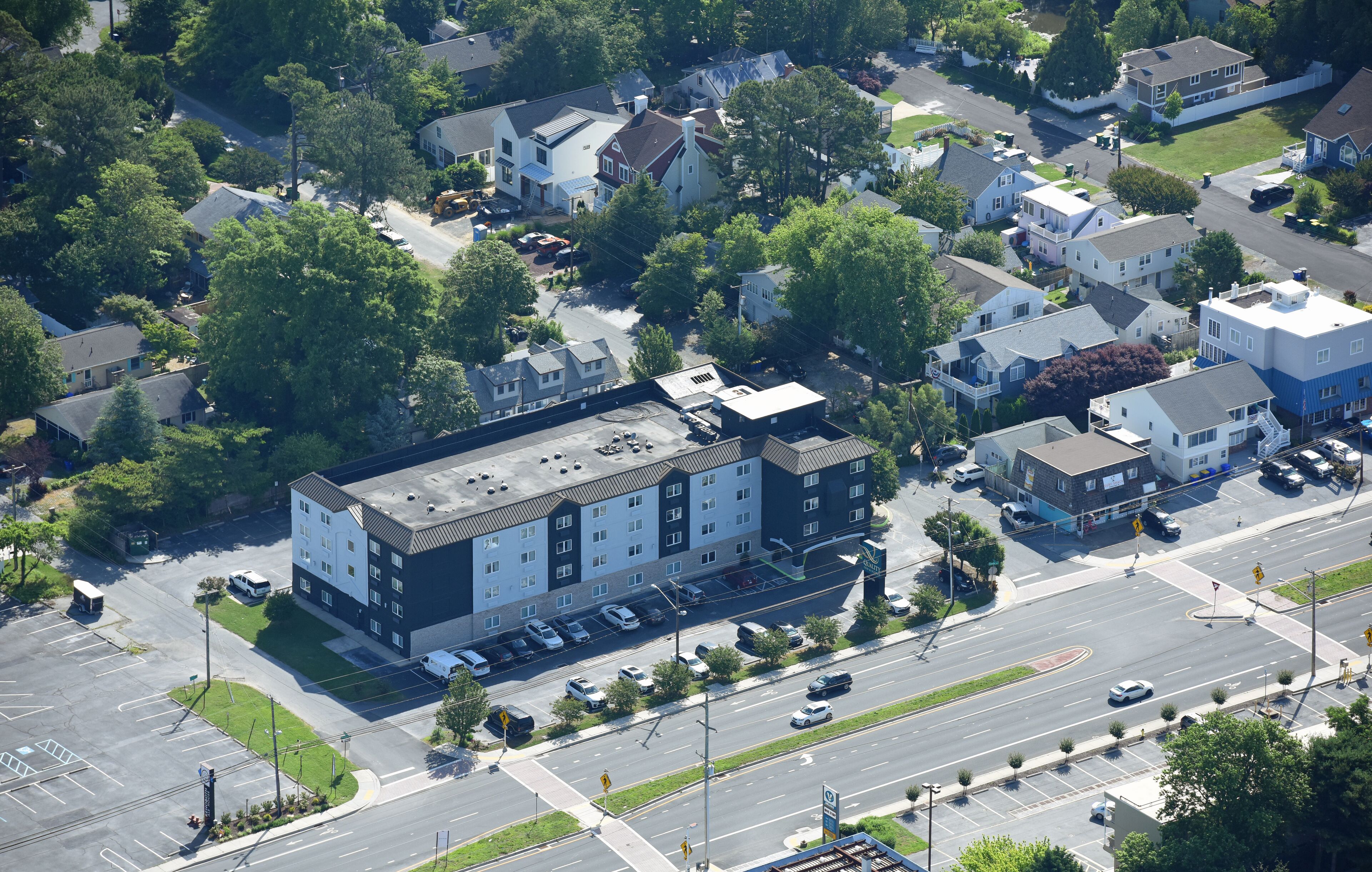 An aerial view of a residential area with a large multi-story building featuring a parking lot and a road intersection.
