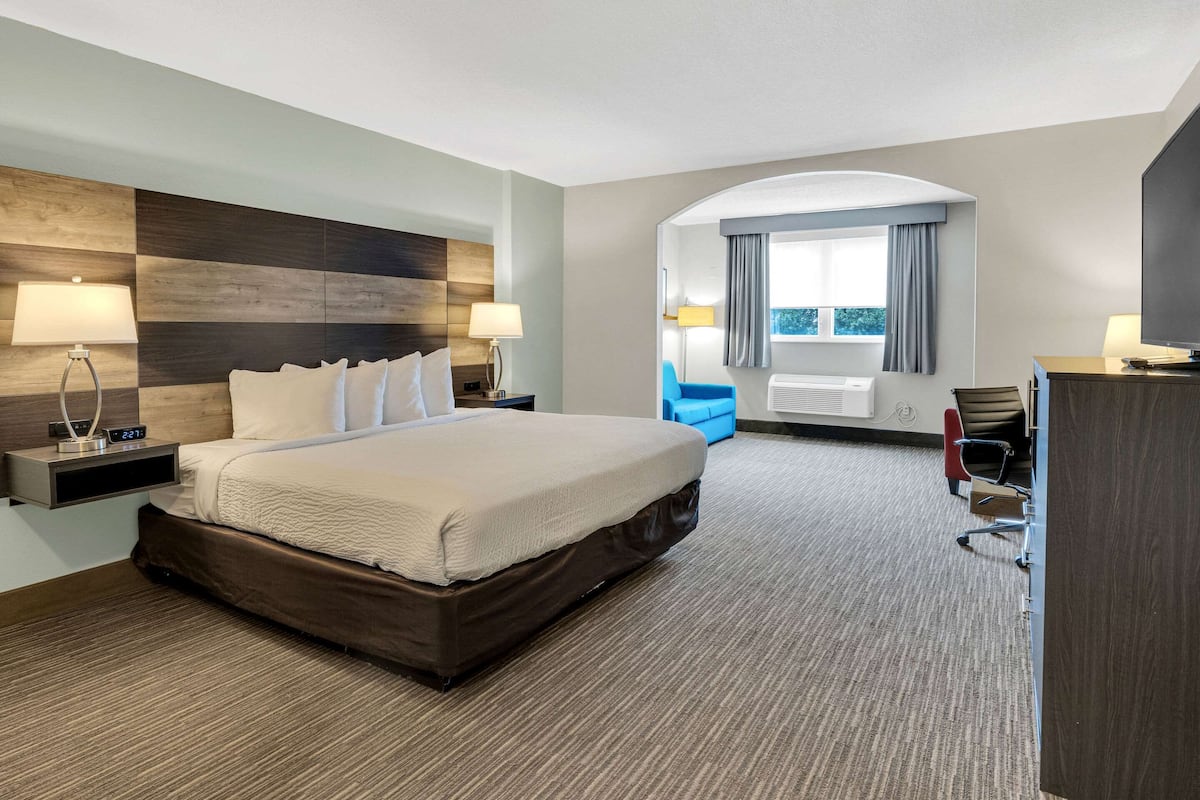 A hotel room with a large bed, a desk with a chair, a TV, and a window with curtains.