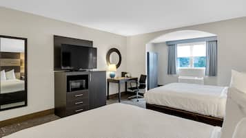 A hotel room with two beds, a desk with a chair, a television, a microwave, and a large window with curtains.