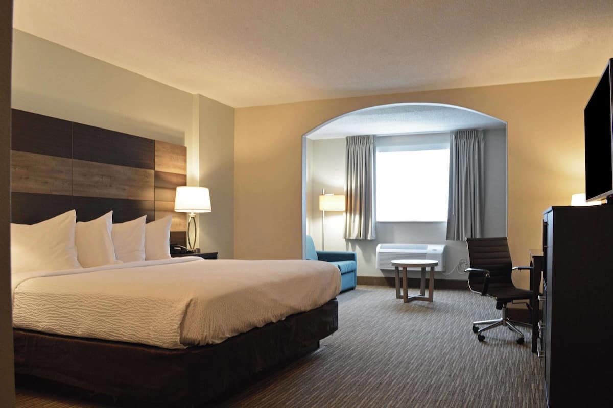 A hotel room with a large bed, a desk, a chair, and a TV.