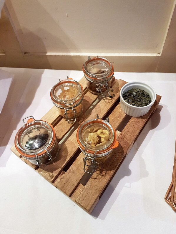 A wooden board with four glass jars containing different food items and a small white bowl with seeds.