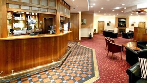 A hotel lobby with a reception desk, seating area, and a patterned floor.