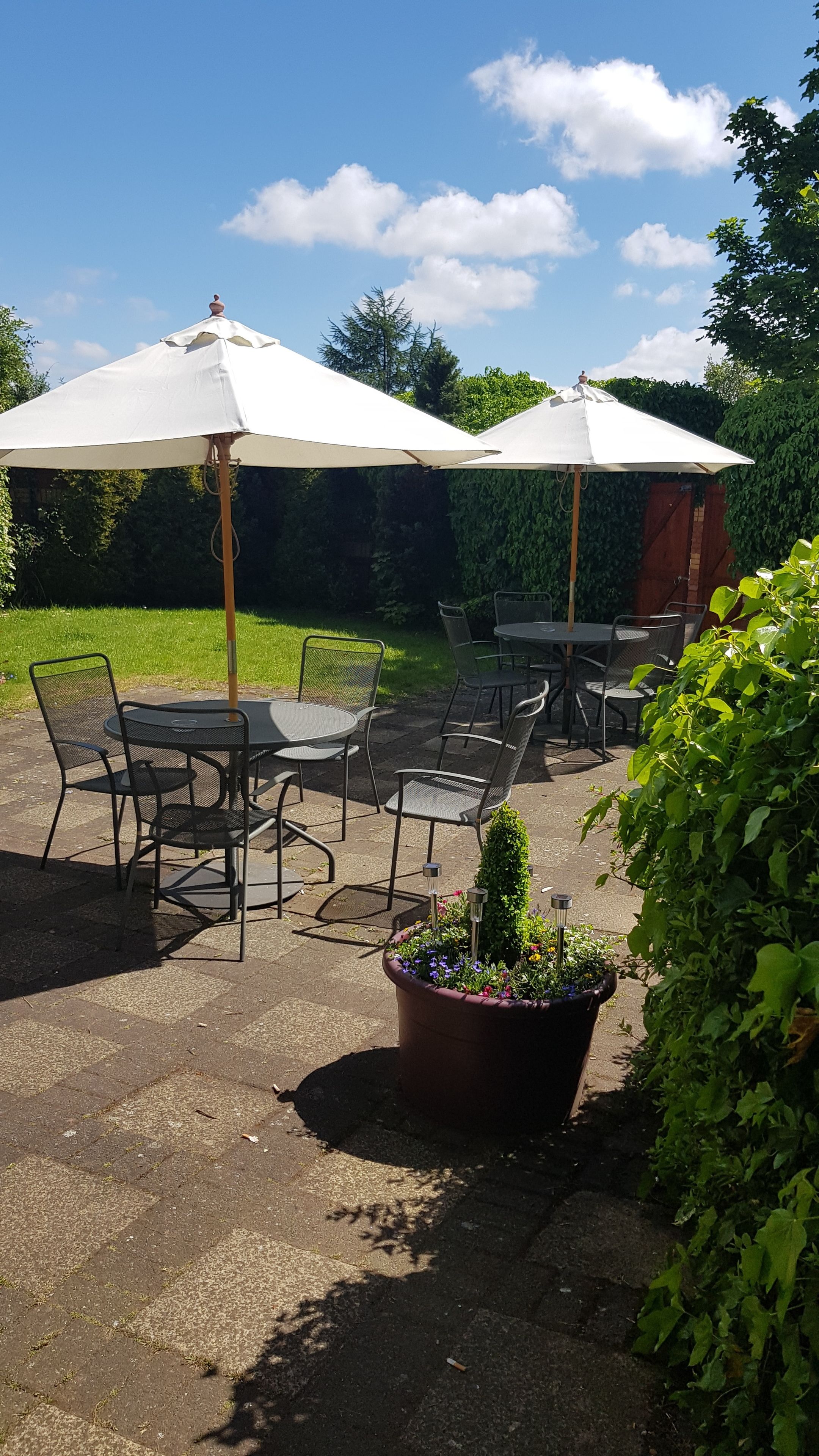 An outdoor patio area with round tables and chairs, two white umbrellas, and a potted plant with colorful flowers.