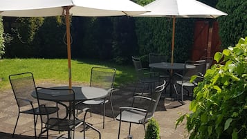 An outdoor patio area with round tables and chairs, two white umbrellas, and a potted plant with colorful flowers.