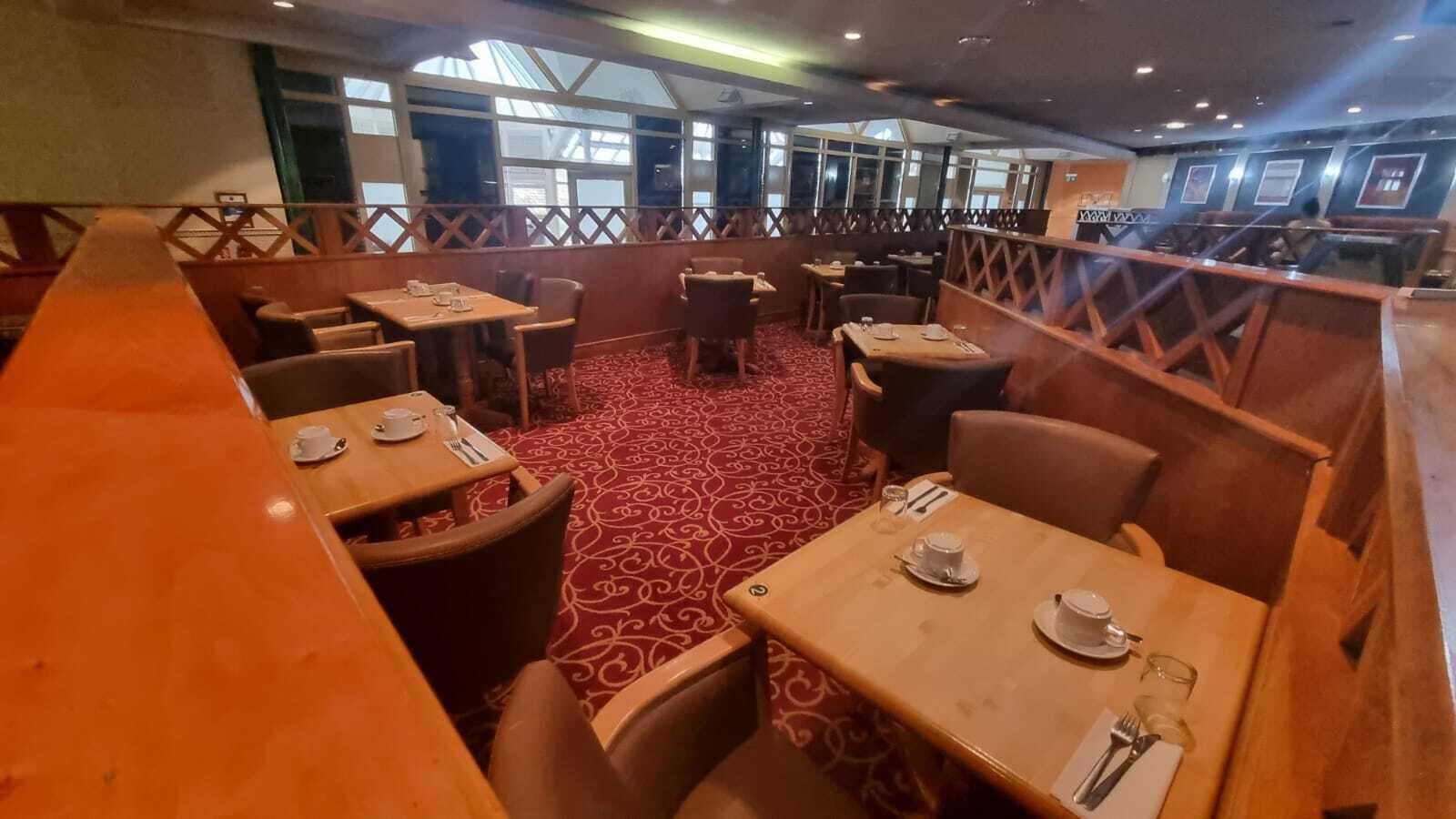 A restaurant with booths and tables, red patterned carpet, and large windows.