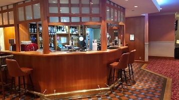 Zona de bar con mostrador de madera, taburetes y suelo a cuadros.