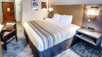 A hotel room with a large bed, a chair, a nightstand with a lamp, and a wall clock.