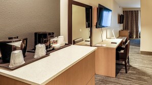 Quarto de hotel com cozinha compacta, um espelho grande, televisão de tela plana e área de estar com vista para o quarto.