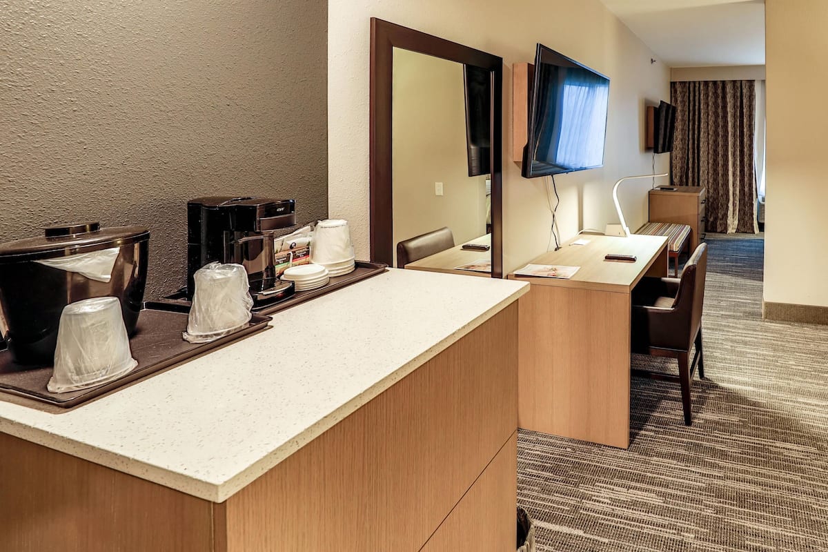 A hotel room with a kitchenette, a large mirror, a flat-screen TV, and a seating area with a view of the room.