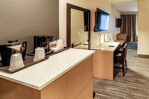 A hotel room with a kitchenette, a large mirror, a flat-screen TV, and a seating area with a view of the room.