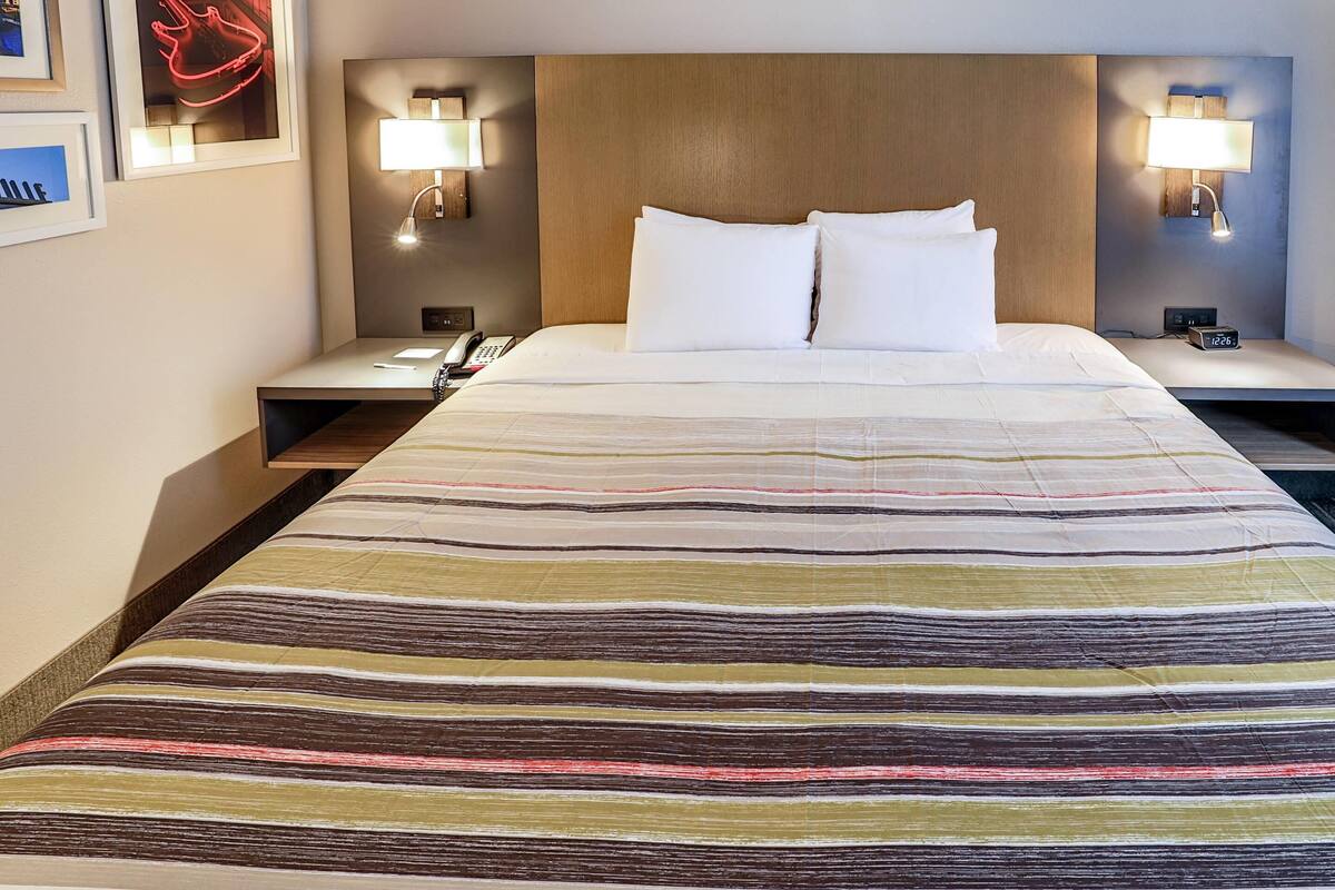 A hotel room with a large bed, two bedside tables, and two wall-mounted lamps.