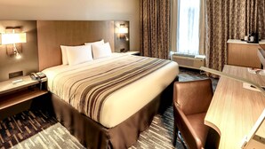 Quarto de hotel com cama grande, abajures, escrivaninha, cadeira e janela com cortinas.