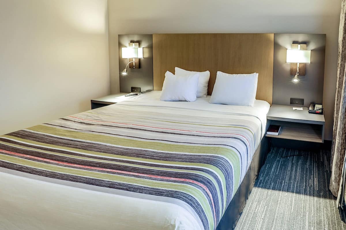 A hotel room with a large bed, two bedside tables, a nightstand, a lamp, and a telephone.
