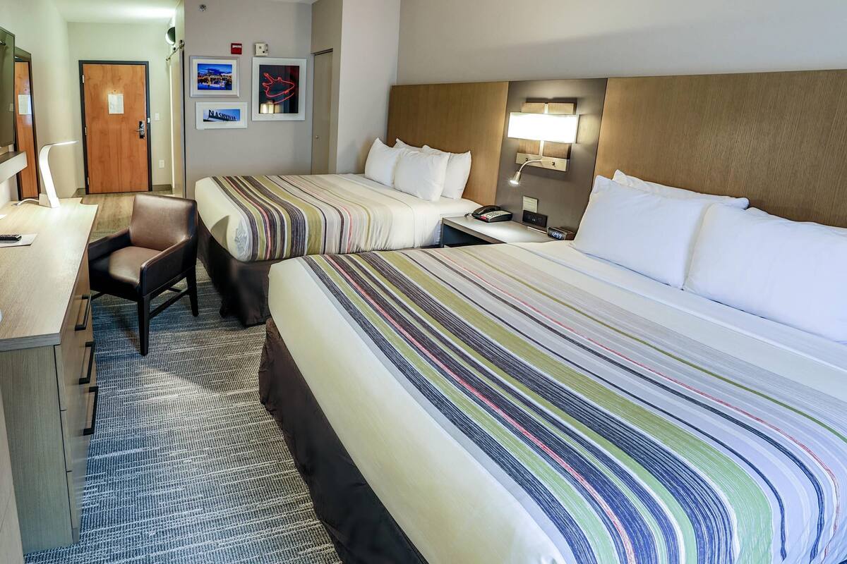 A hotel room with two beds, a desk, and a chair.