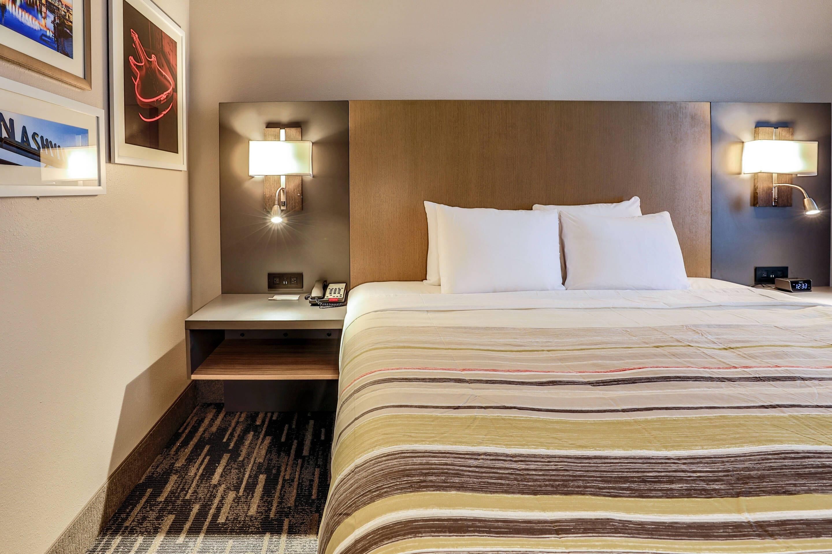A hotel room with a large bed, two bedside lamps, a nightstand with a phone, and framed pictures on the wall.